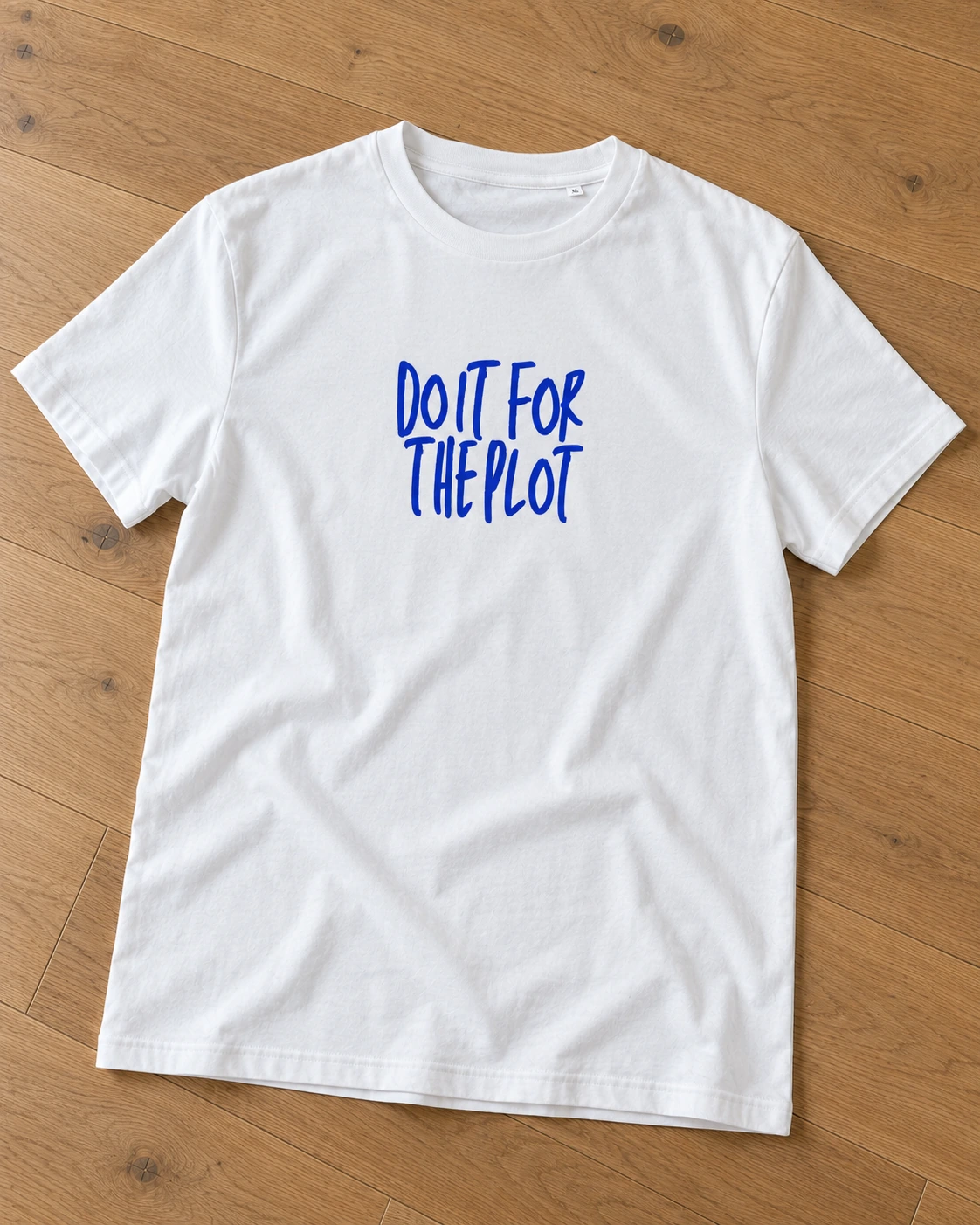 Balts T-krekls “Do it for the plot” uz koka grīdas